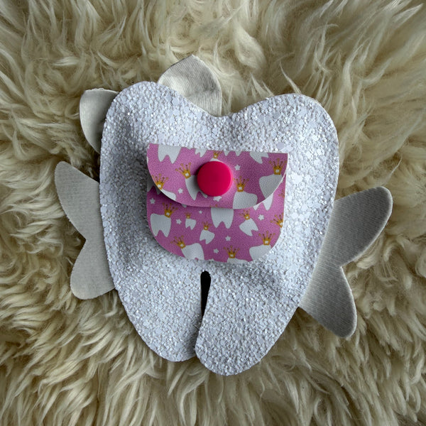 White tooth-shaped pillow with a pink fabric heart on a fluffy white surface