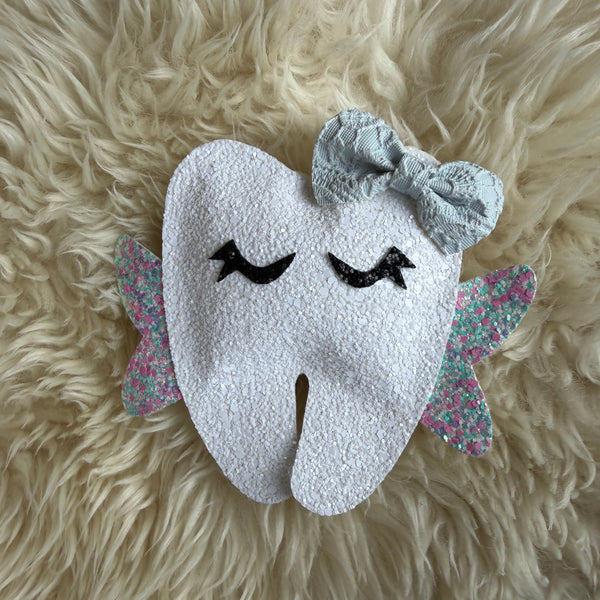 Tooth-shaped plush toy with a bow on a fluffy beige surface