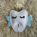 Decorative tooth-shaped pillow with a gold crown on a fluffy beige surface