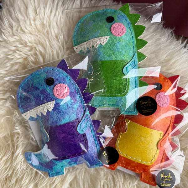 Three colorful dinosaur toys in clear packaging on a fluffy white surface