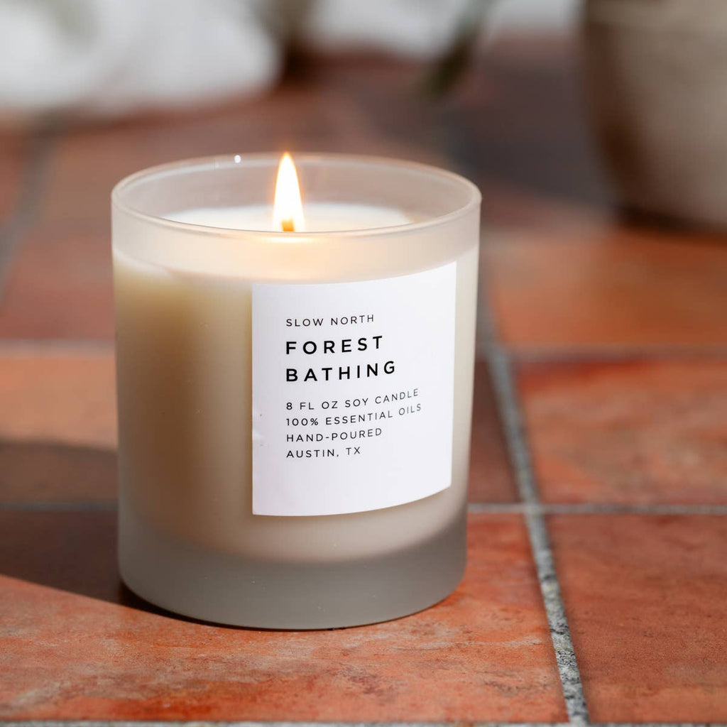 Candle labeled 'Forest Bathing' on a tiled surface with a plant in the background
