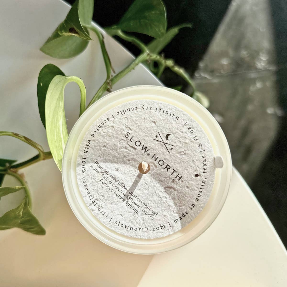 Round product with 'Slow North' branding on a white surface with green leaves in the background