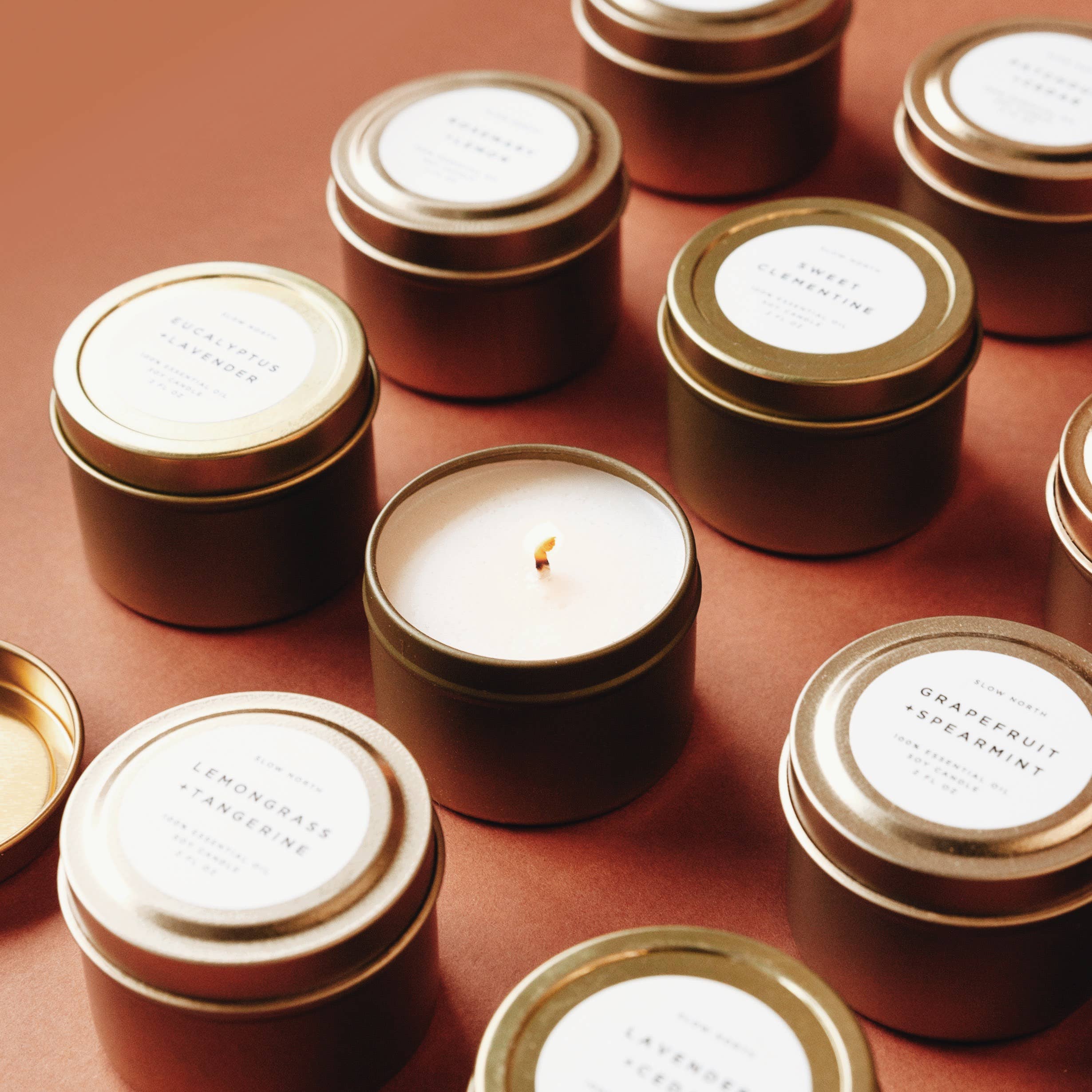 Collection of candles in gold tins with labels on a brown surface