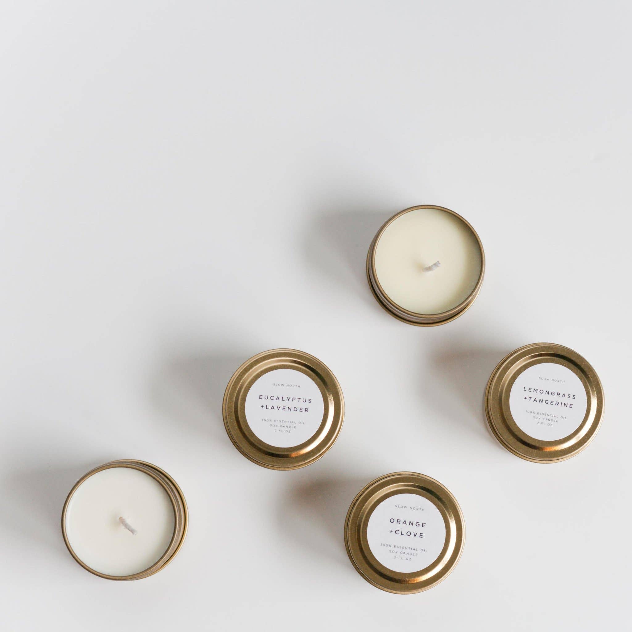 Five small candles in gold tins with labels on a light gray background