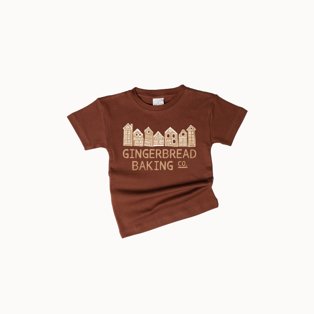 A brown short-sleeve t-shirt with a graphic of gingerbread houses and the text 'GINGERBREAD BAKING CO.' printed in a light tan color, displayed on a clean white background.