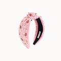 A pink velvet knotted headband embellished with faux pearls, rhinestones, and small gingerbread men charms, shown against a plain off-white background.