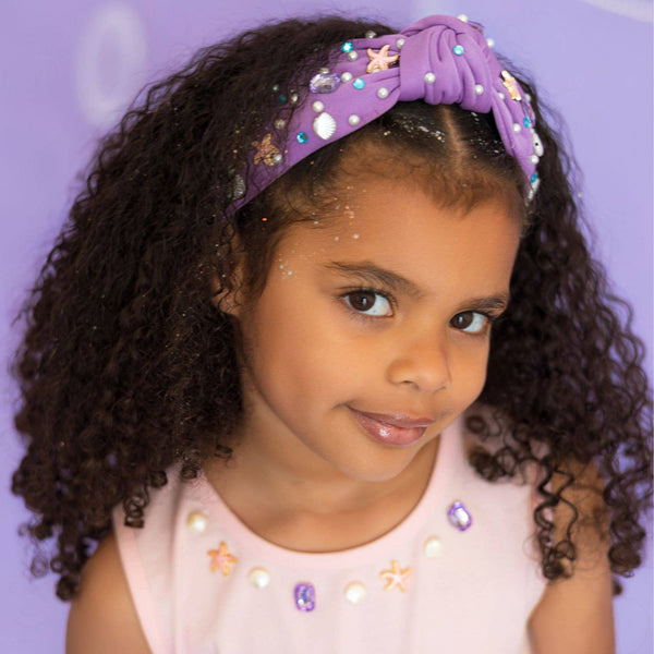 Young girl wearing a purple headband with decorative elements on a purple background
