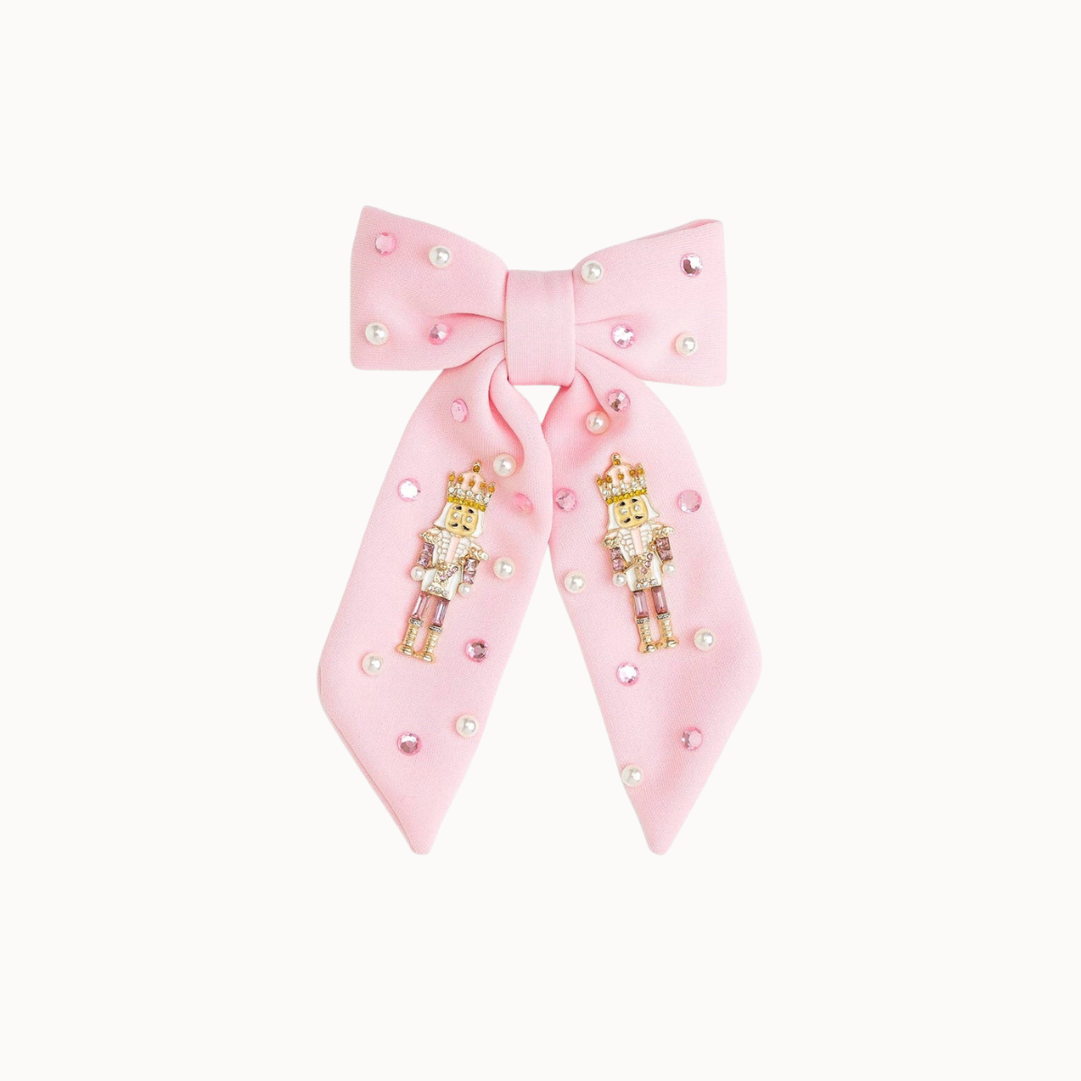 A light pink bow hair accessory embellished with small rhinestones and two gold-toned nutcracker figures, shown on a plain off-white background.