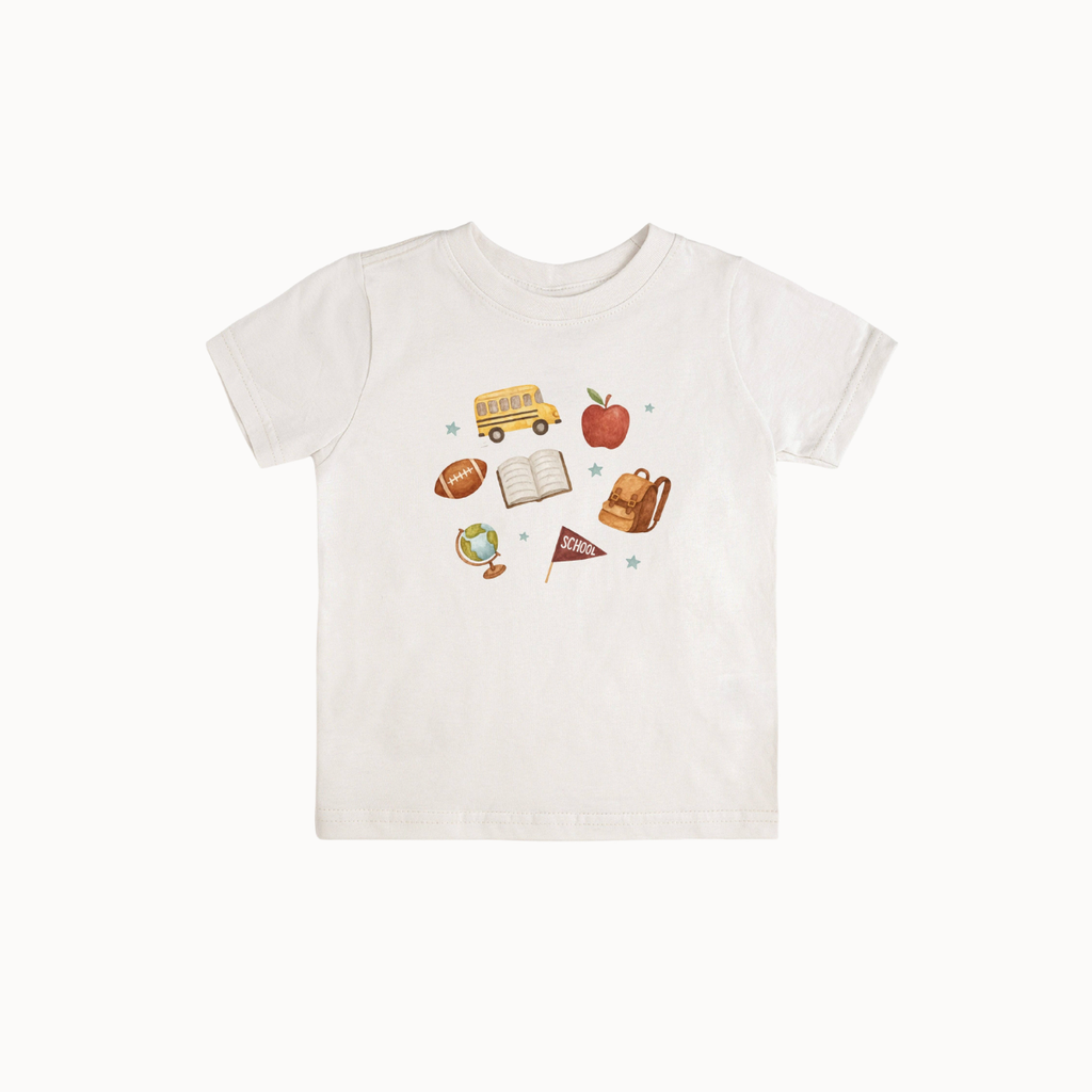 A white short-sleeve baby t-shirt with a colorful school-themed graphic print on the front, featuring illustrations of a yellow school bus, an apple, a football, an open book, a backpack, and a small flag.