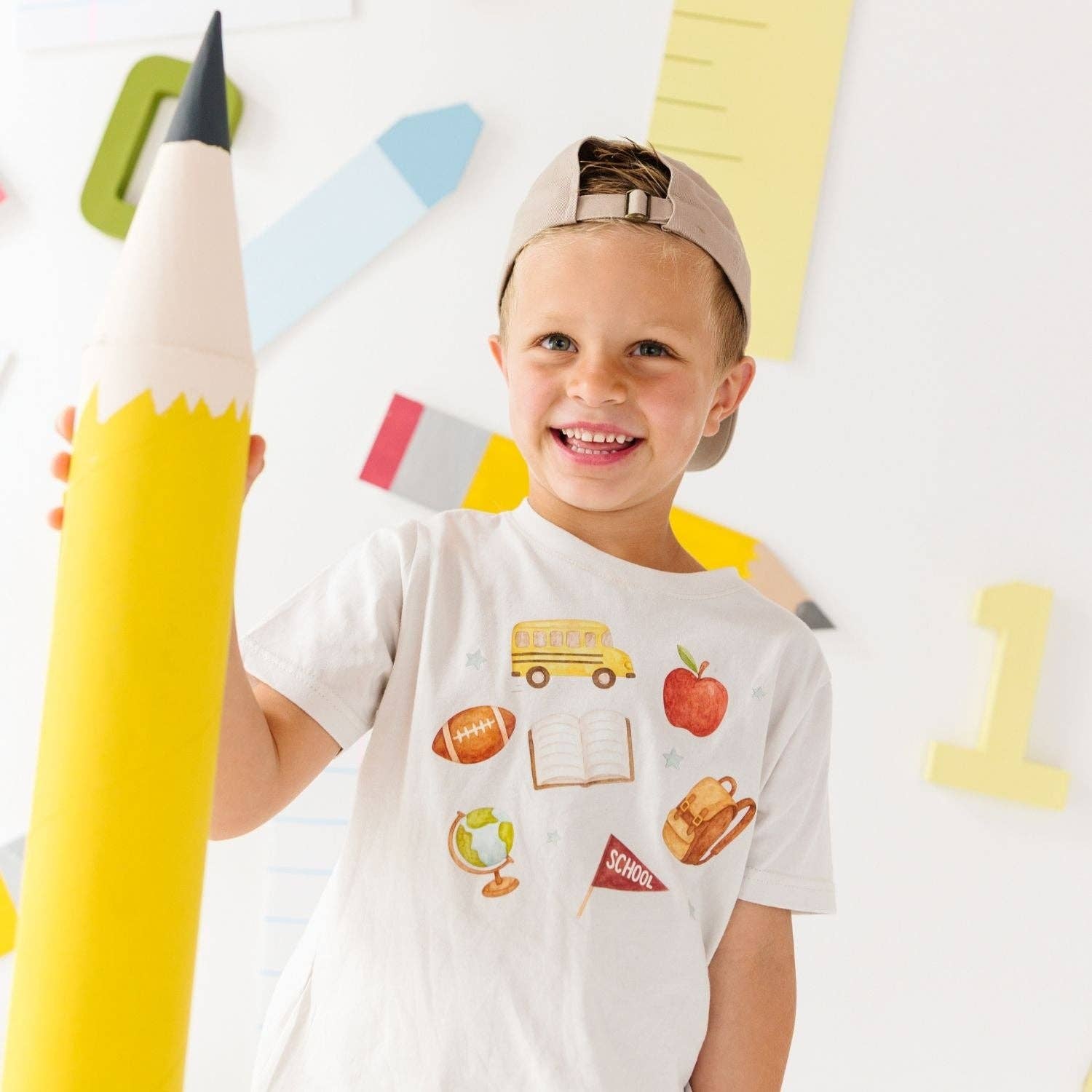 Child holding a large inflatable pencil with colorful stationery items in the background