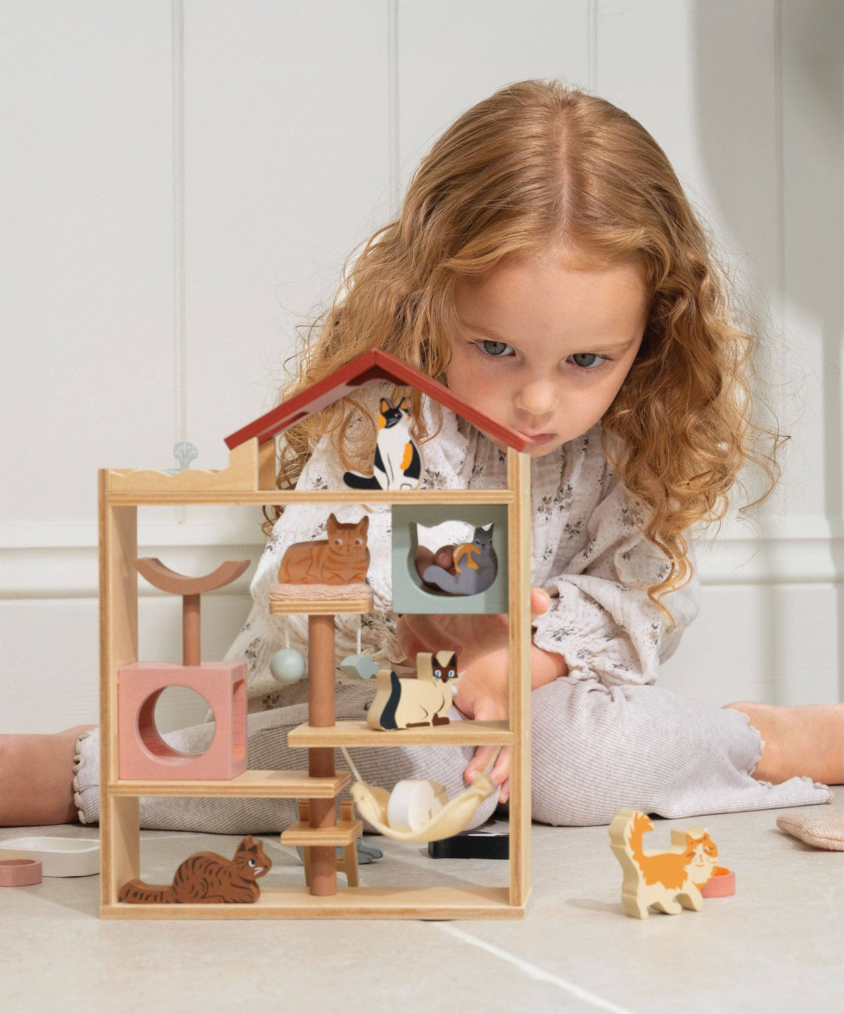 Child playing with a wooden animal playset on a light-colored floor.