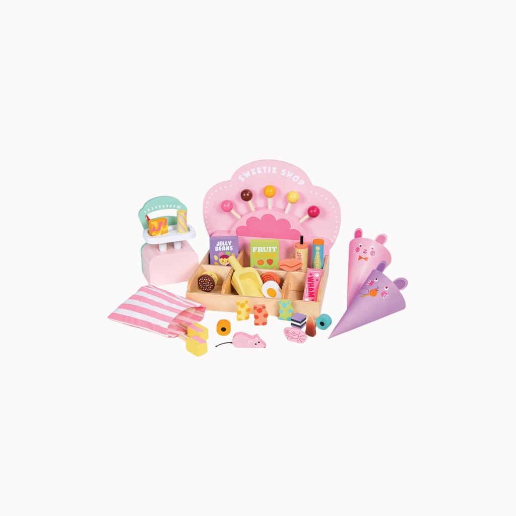 A children's wooden pretend-play toy set styled like a sweet shop, featuring a pink counter, ice cream cone, striped napkin, and assorted colorful food and drink accessories on a plain white background.