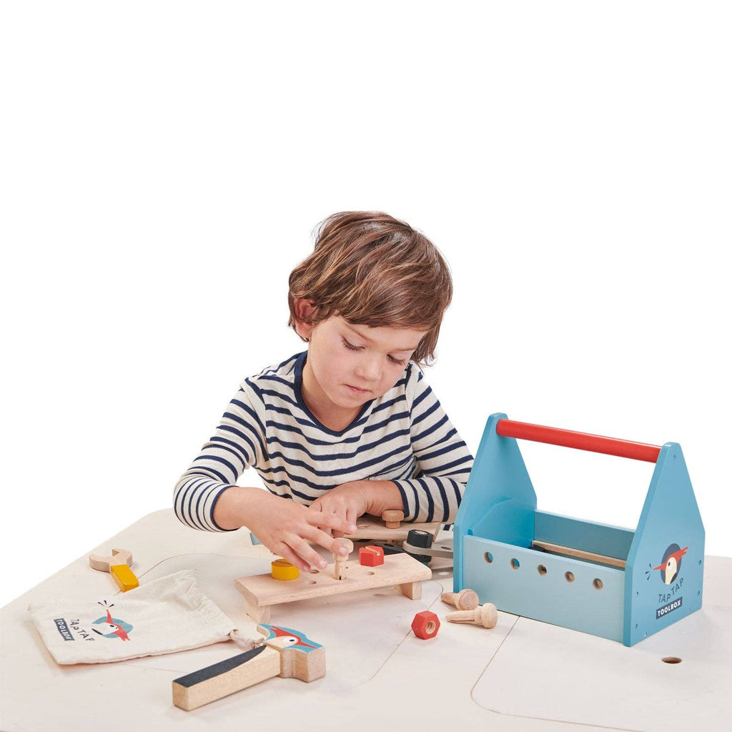 Child playing with a wooden tool set on a white surface