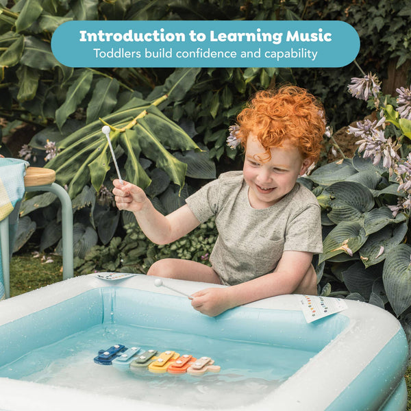 Child playing with musical instruments in a small pool outdoors, with text about learning music.