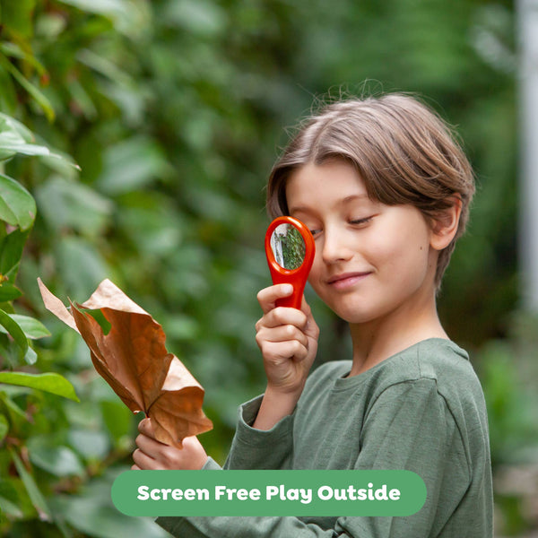 Child holding a red magnifying glass to a leaf with a green background