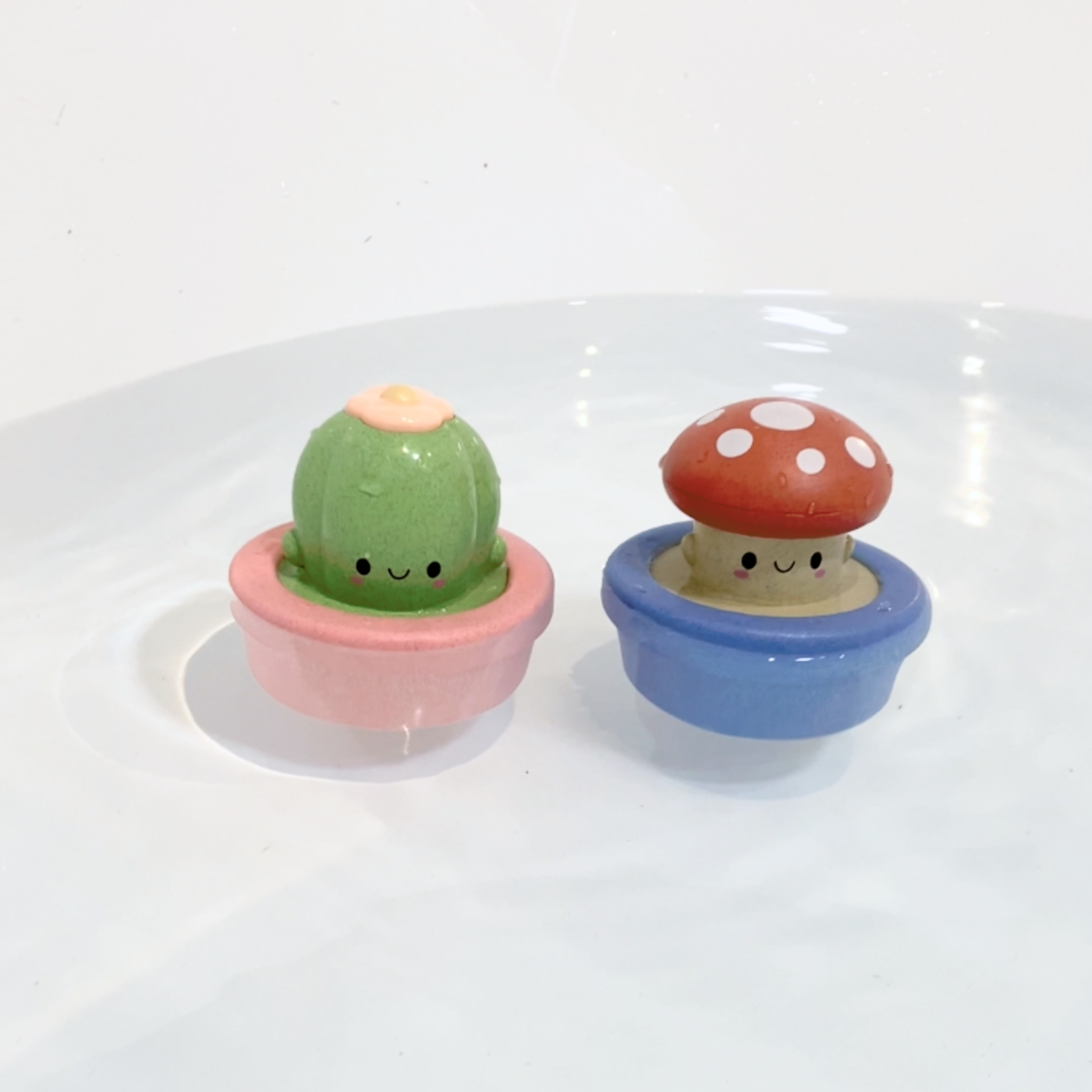 Two small ceramic figurines, one resembling a cactus and the other a mushroom, on a white background.