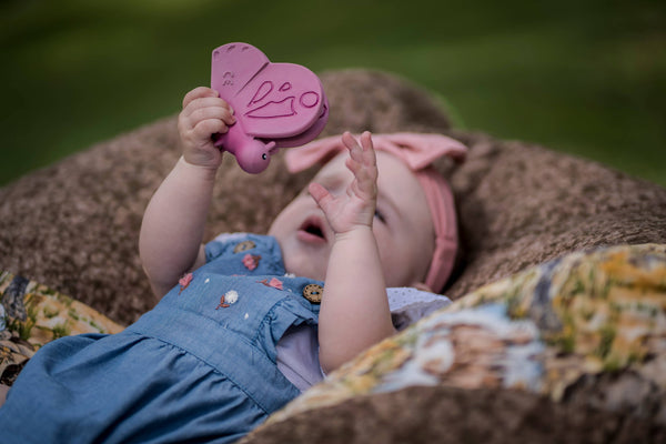 Baby lying on a floral blanket holding a pink butterfly toy.