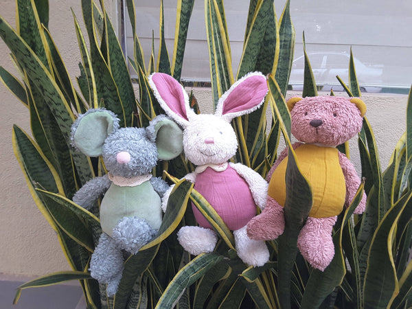 Three plush toys (mouse, rabbit, bear) in front of a plant