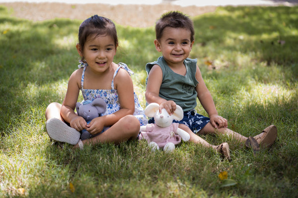 Two children sitting on grass with stuffed animals