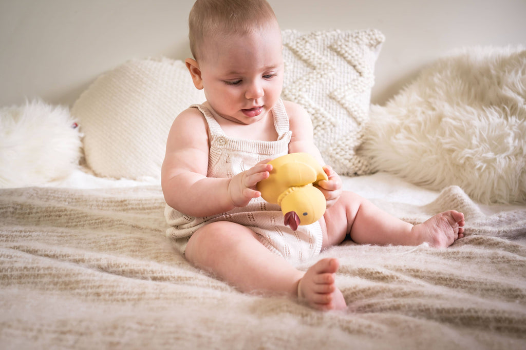 Baby playing with a yellow rubber duck on a soft surface