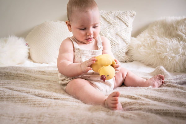 Baby playing with a yellow rubber duck on a soft surface