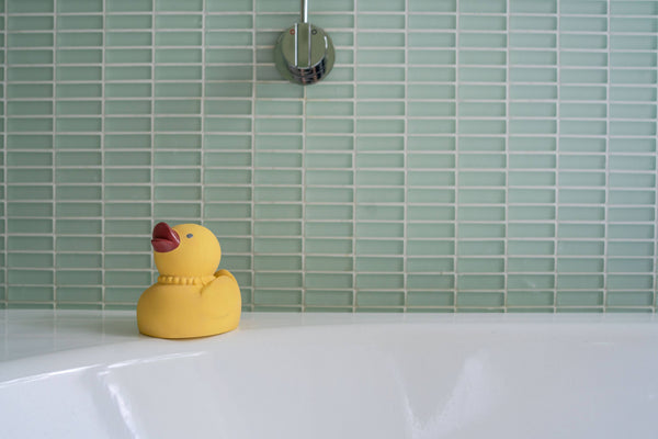 Yellow rubber duck on a white bathtub with green tiled wall