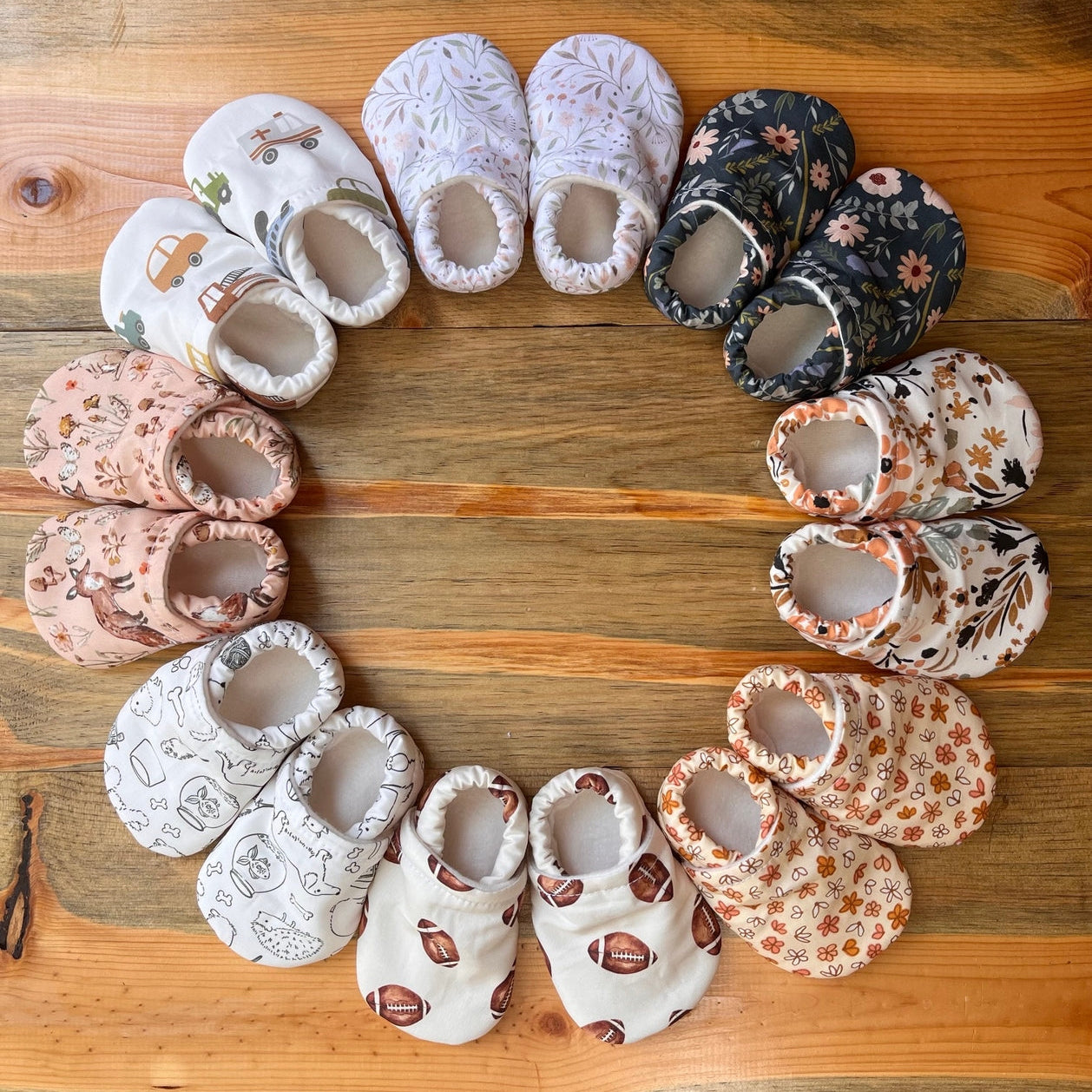 Assorted baby shoes arranged in a circular pattern on a wooden surface