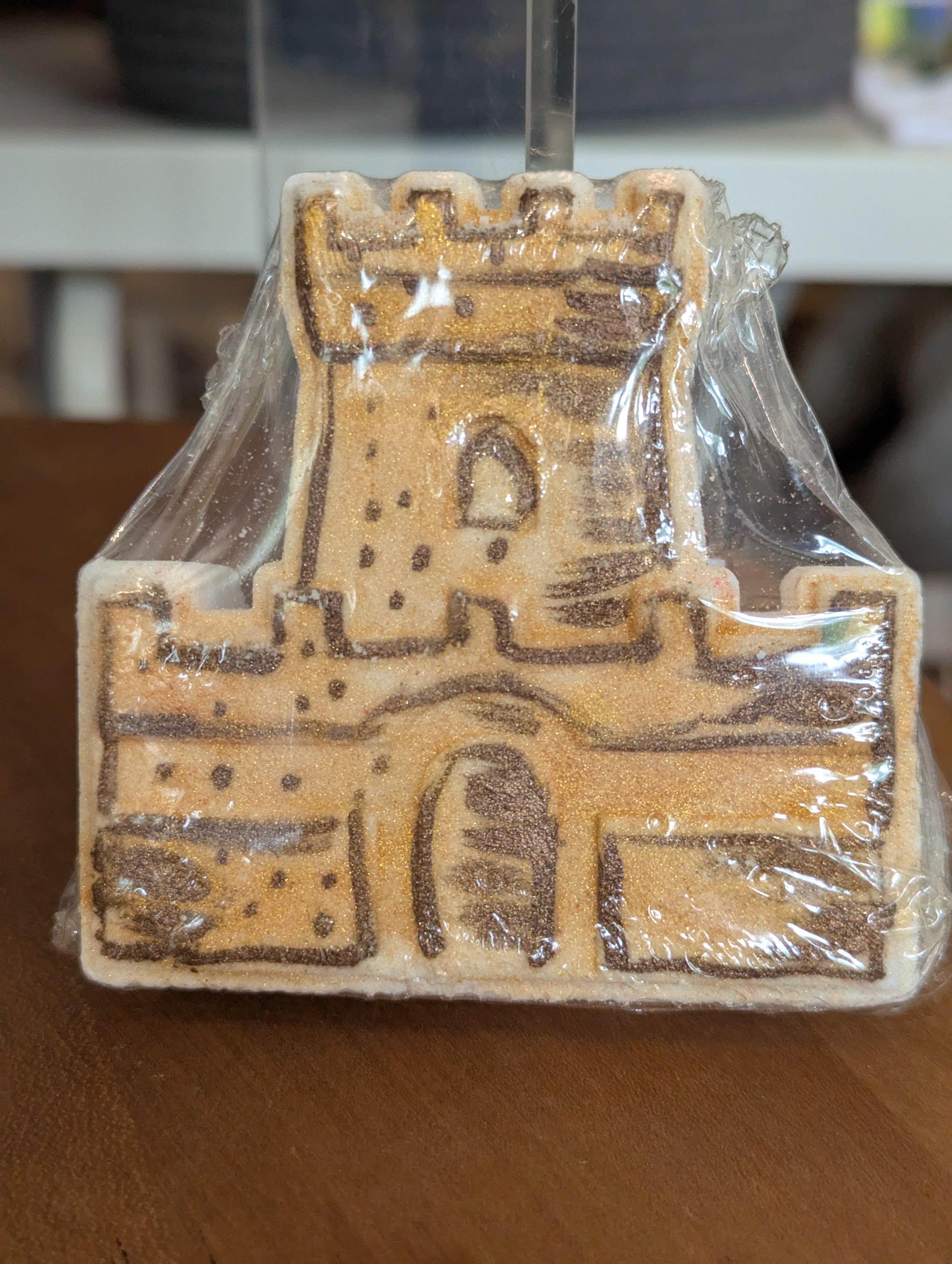Baked castle-shaped bath bomb in a clear plastic bag on a wooden surface