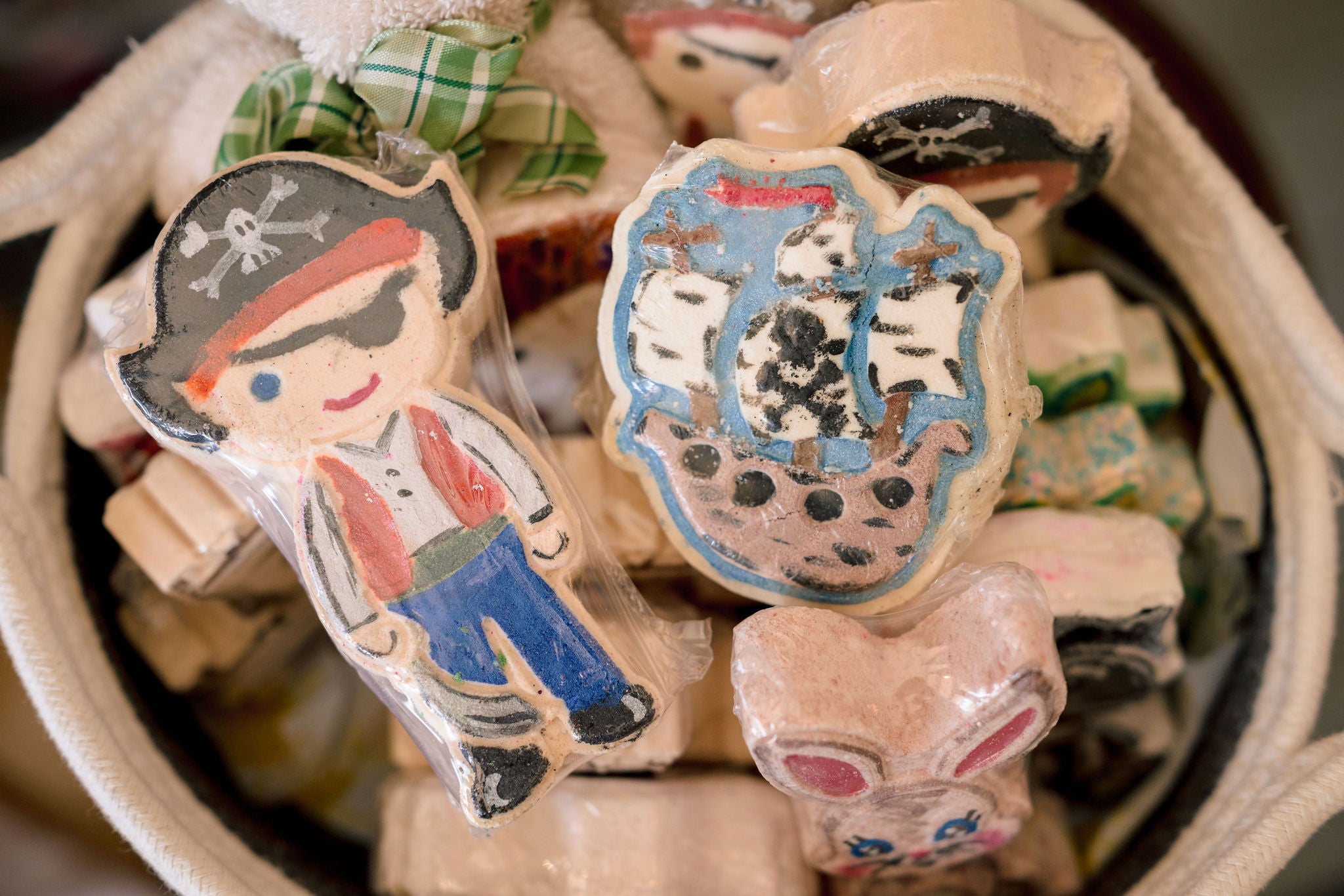 A close-up of a basket filled with small wooden pirate-themed figurines or ornaments, including a standing pirate figure and a ship-shaped piece, with some wrapped in clear plastic.
