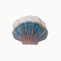 A small shell-shaped decorative object with a blue, purple, and gold fan-like pattern on a plain white background.