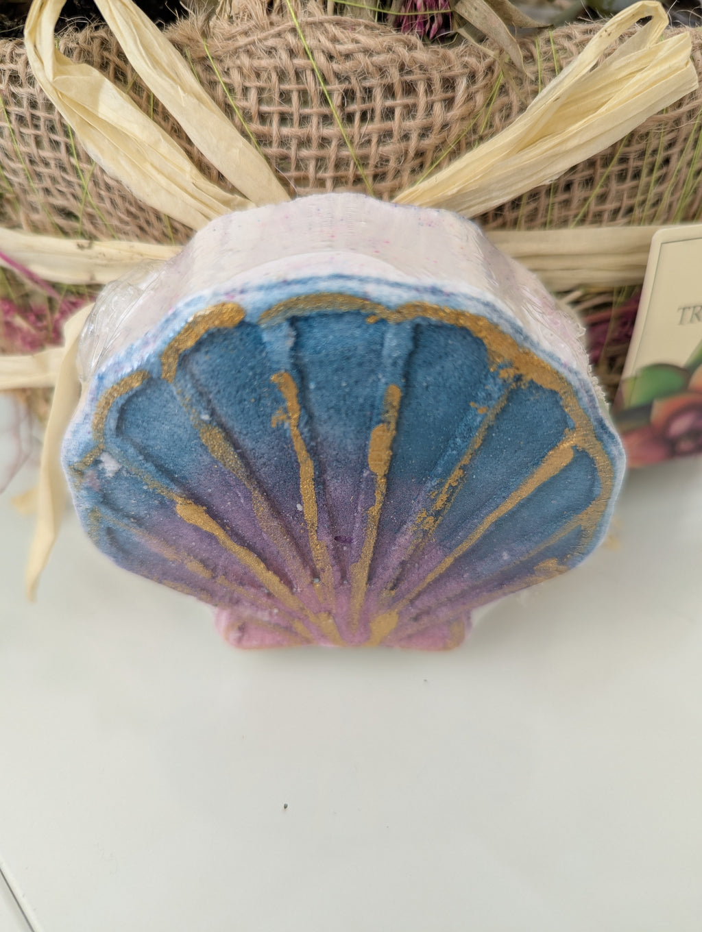 Shell-shaped bath bomb with blue and gold design on a white surface