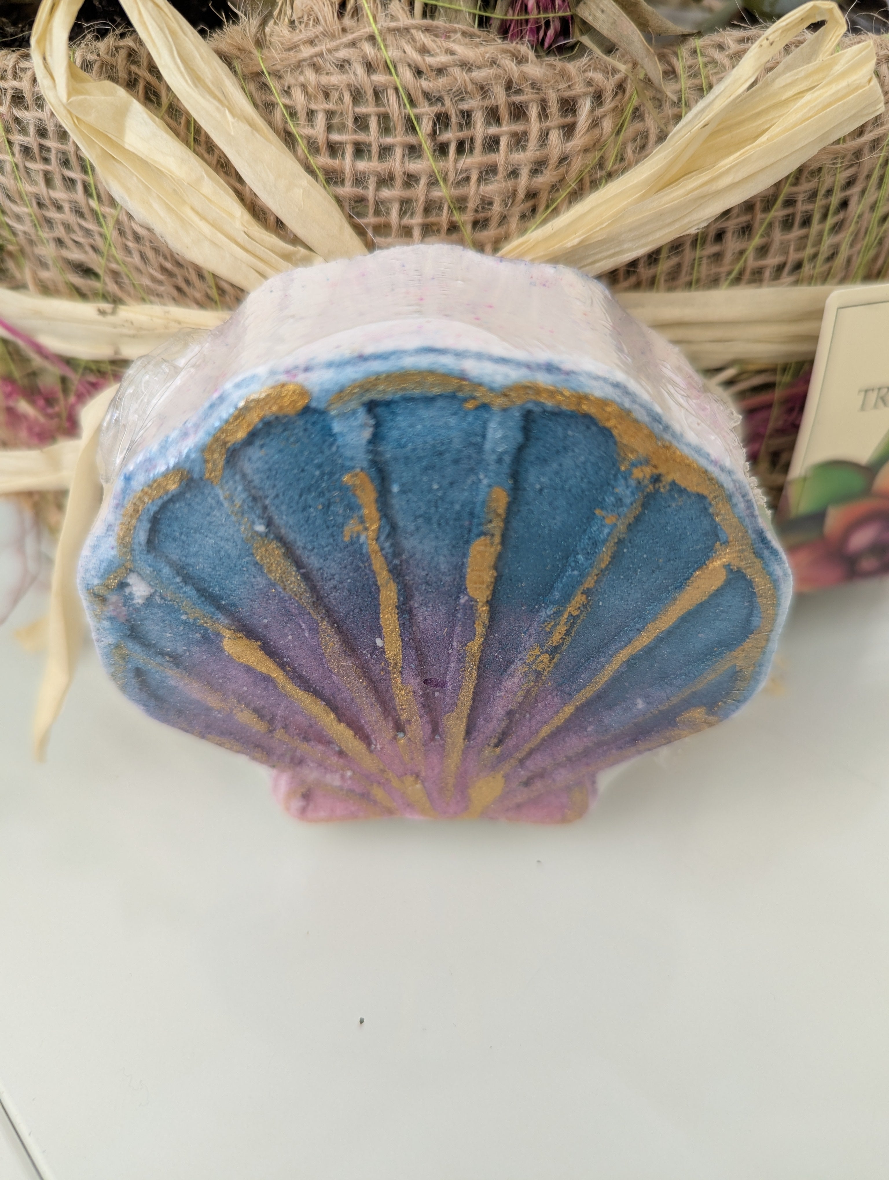 Shell-shaped bath bomb with blue and gold design on a white surface