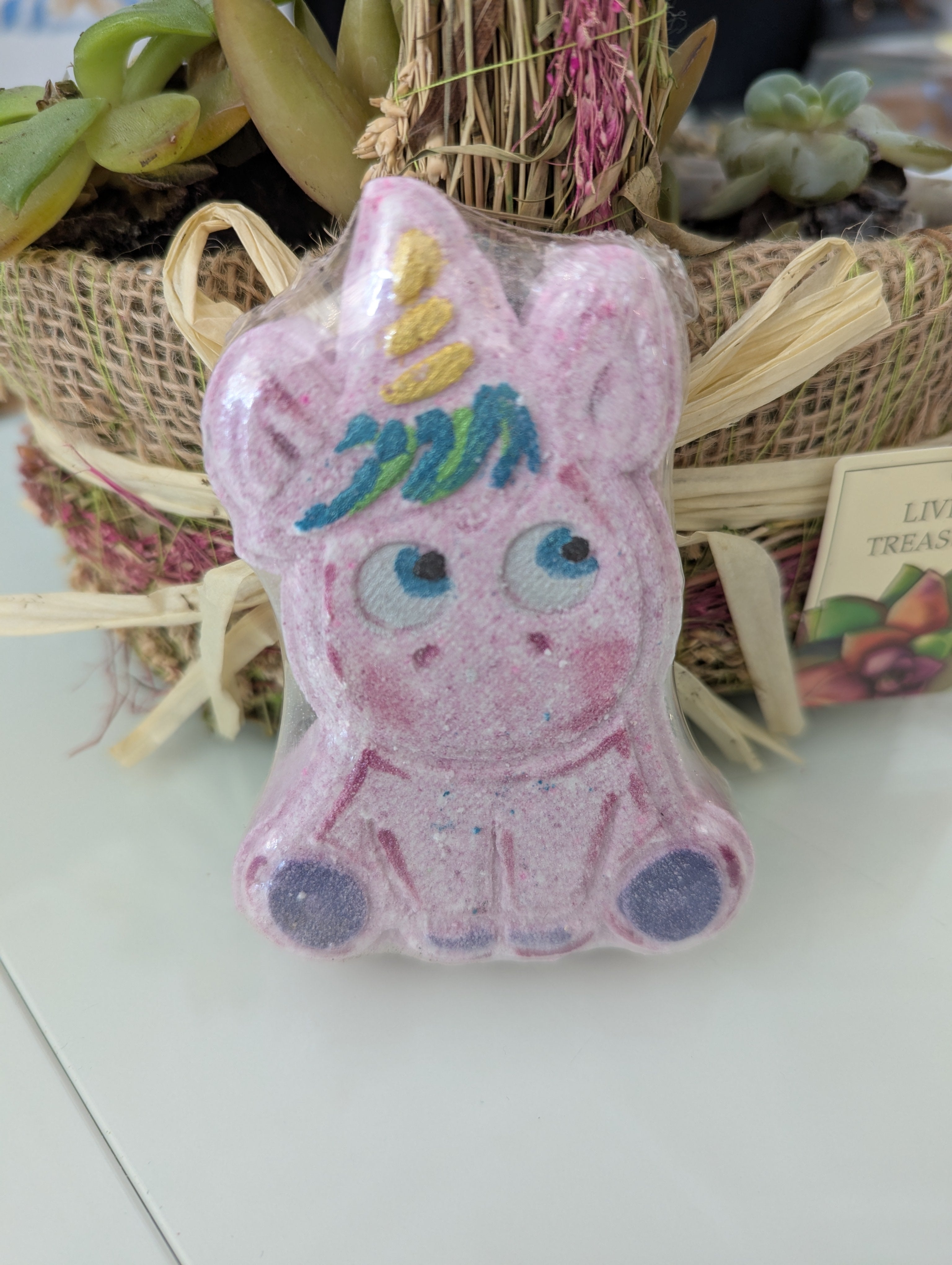 Pink unicorn bath bomb with colorful mane on a white surface