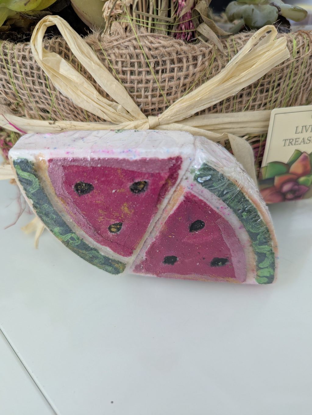 Watermelon-themed bath bomb with a decorative bow on a white surface