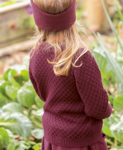 A girl wearing a maroon, crew neck, long-sleeved pullover sweater with a traditional zigzag pattern.
