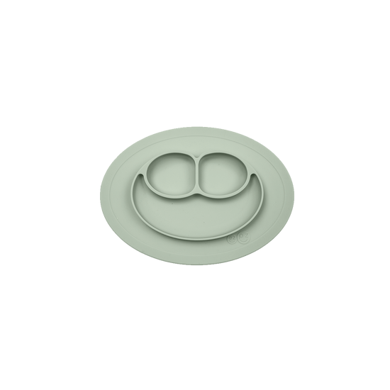 A green ezpz Mini Mat, an all-in-one placemat and plate designed for mealtime, suctioning to a table surface.