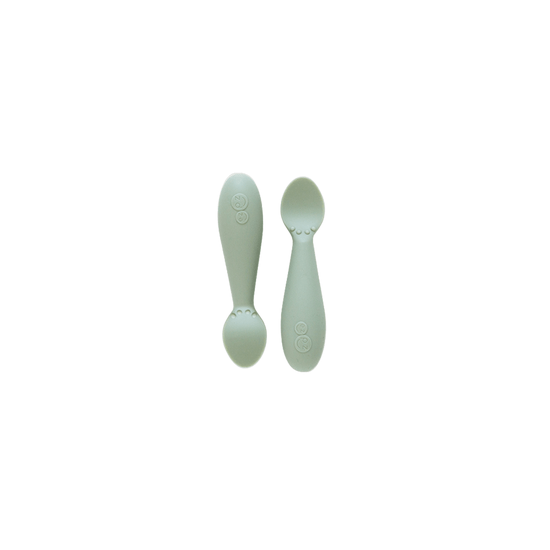 Two white silicone spoons designed for babies, with wide handles and narrow bowls.