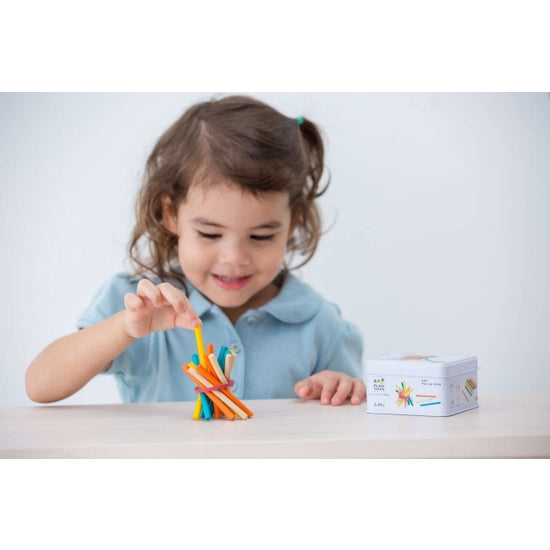 A child playing with PlanToys Pick Up Sticks, a game that involves removing colorful sticks from a box, enhancing fine motor skills and hand-eye coordination.