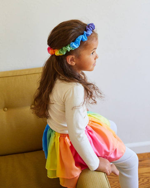 child wearing a rainbow headband and skirt sitting on a couch